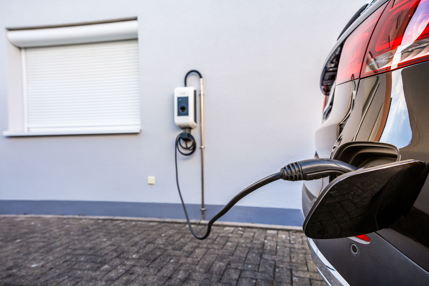 Wallbox an der Fassade eines Einfamilienhauses, E-Auto parkt daneben